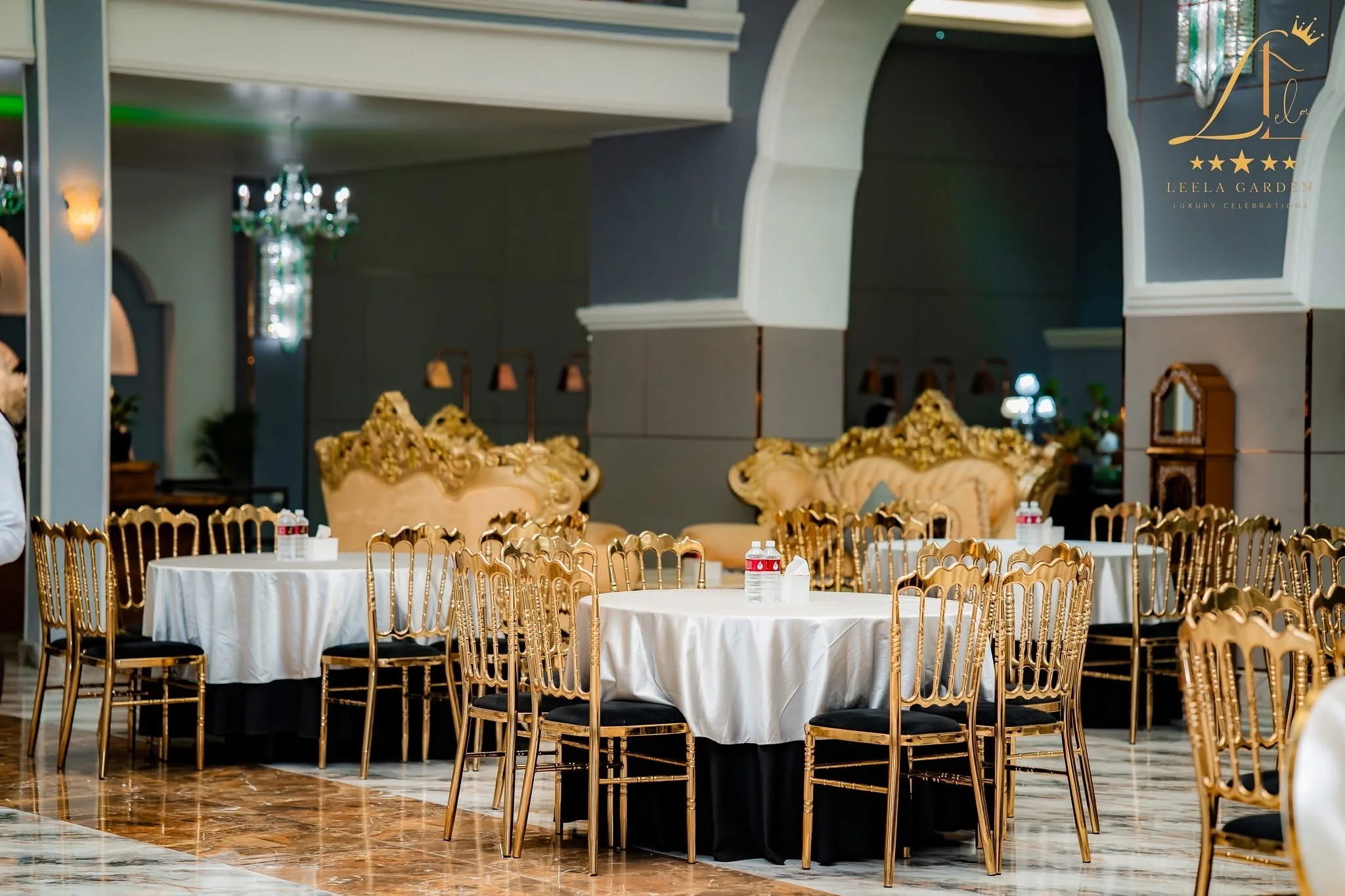 A pair of gilded thrones overlooking dressed round tables in the hall.