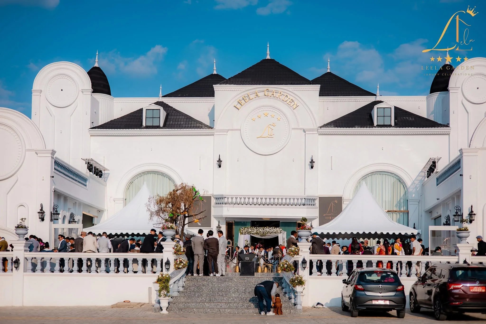The full width of the estate in daylight, guests gathered on the forecourt beside white marquees.