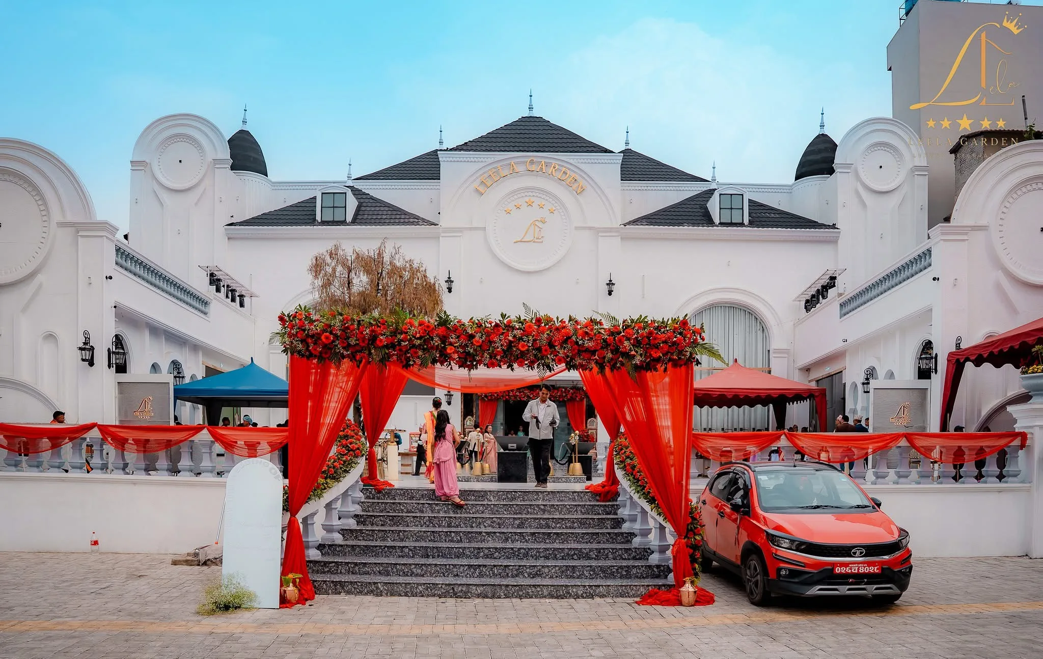 The entrance stair dressed with red drapes and florals for an arrival, a car waiting at the foot.