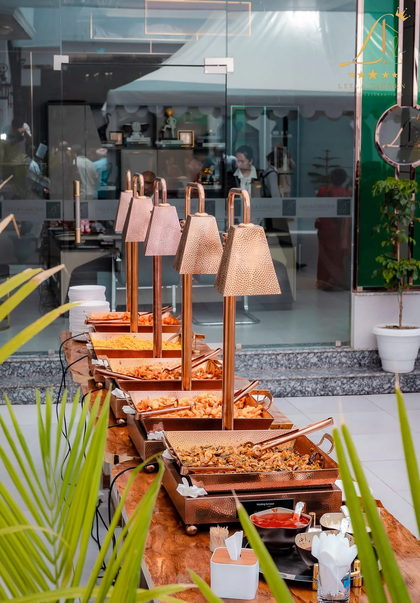 An outdoor service counter with copper lamps, set beside planted greenery.