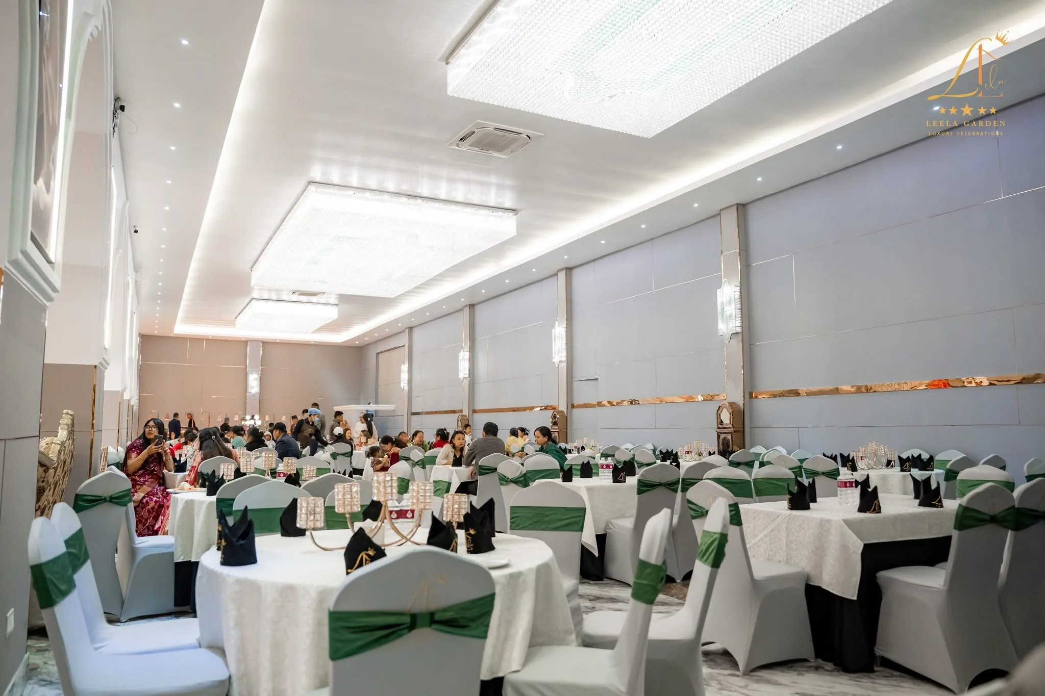 The hall set with white chair covers and green sashes, guests seated at the far tables.