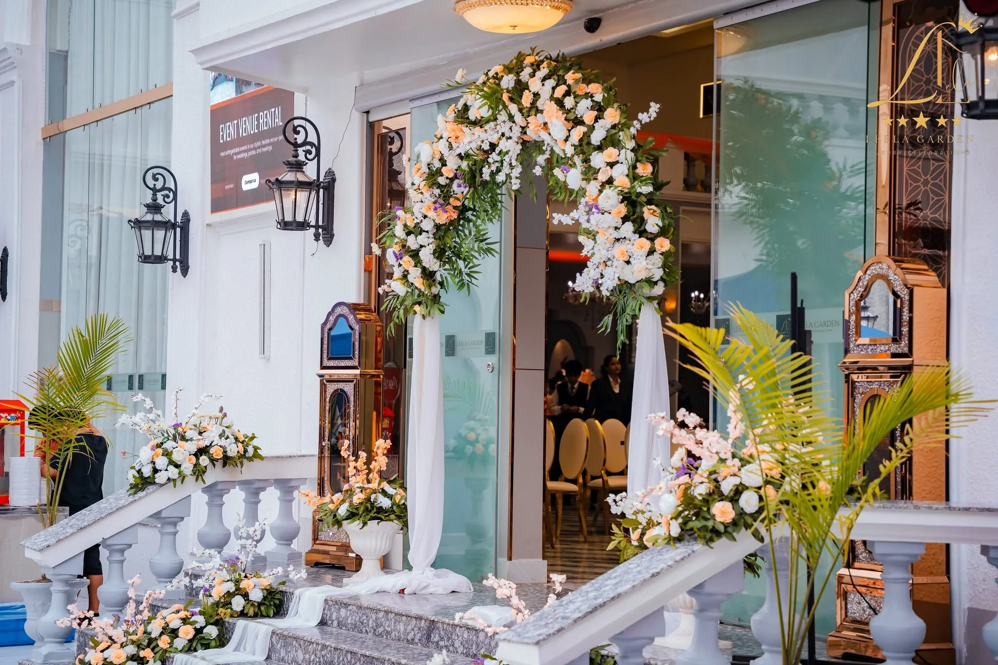 Florals and drapes dressing the entrance, palms flanking the stair into the hall.