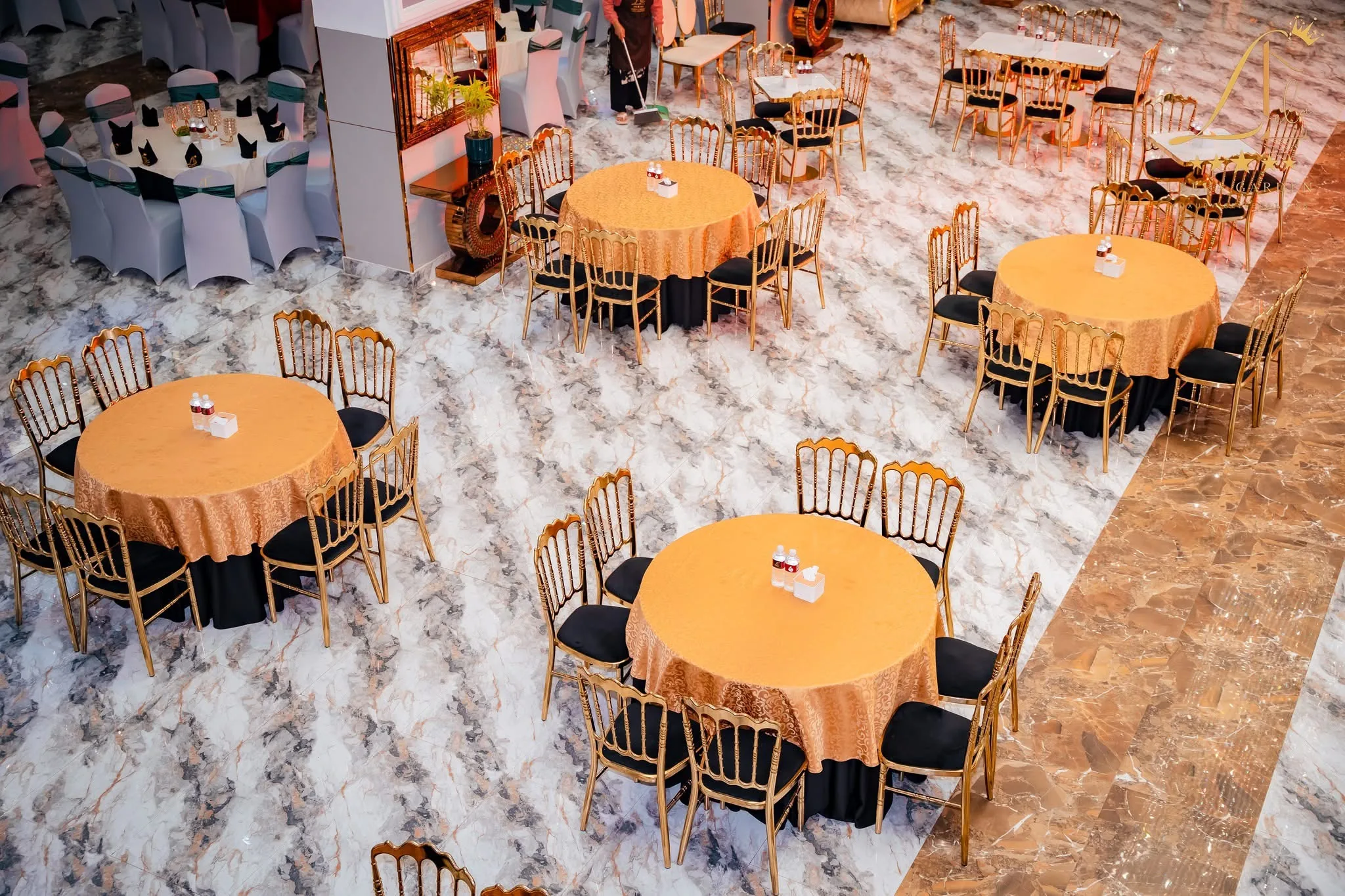 Round tables under orange and gold cloths with gold chiavari chairs, seen from above.