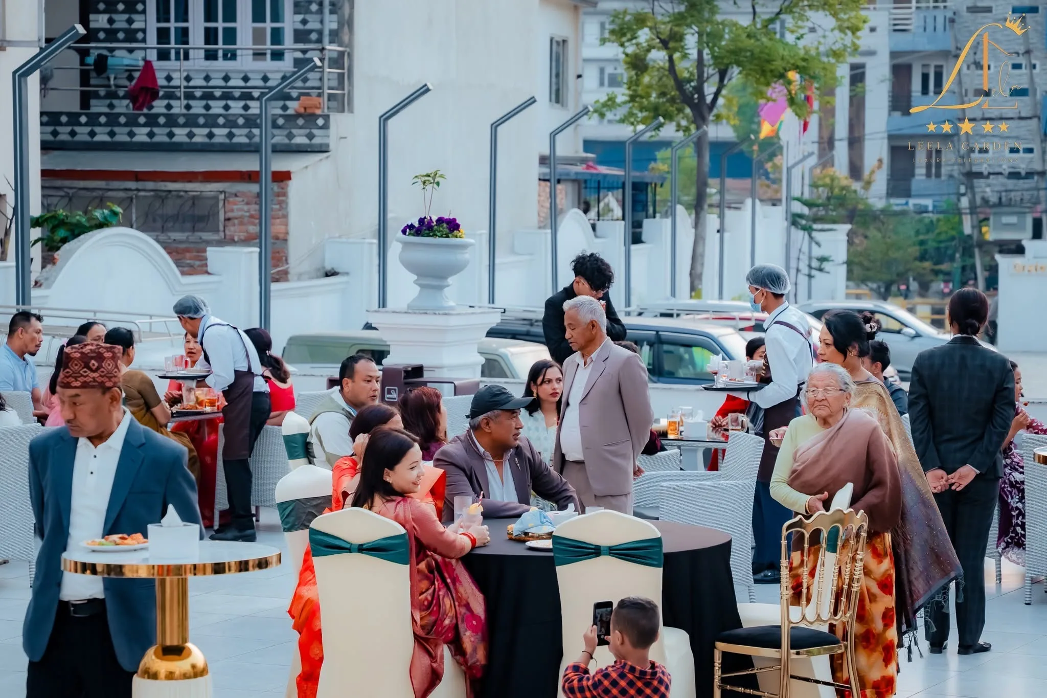 Guests mingling on the forecourt beside planters, cars parked along the drive.