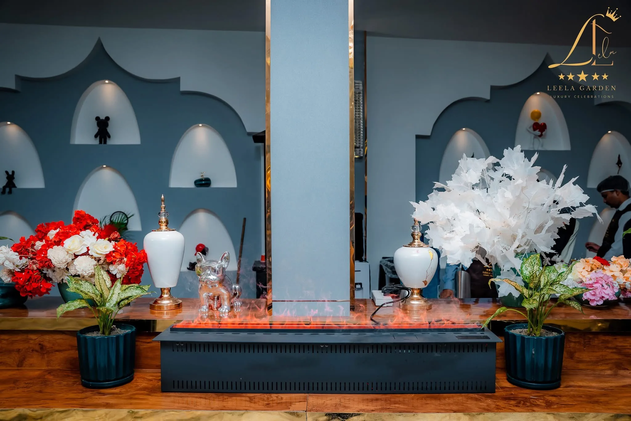 A decorative console between arched blue alcoves, dressed with red and white floral urns.