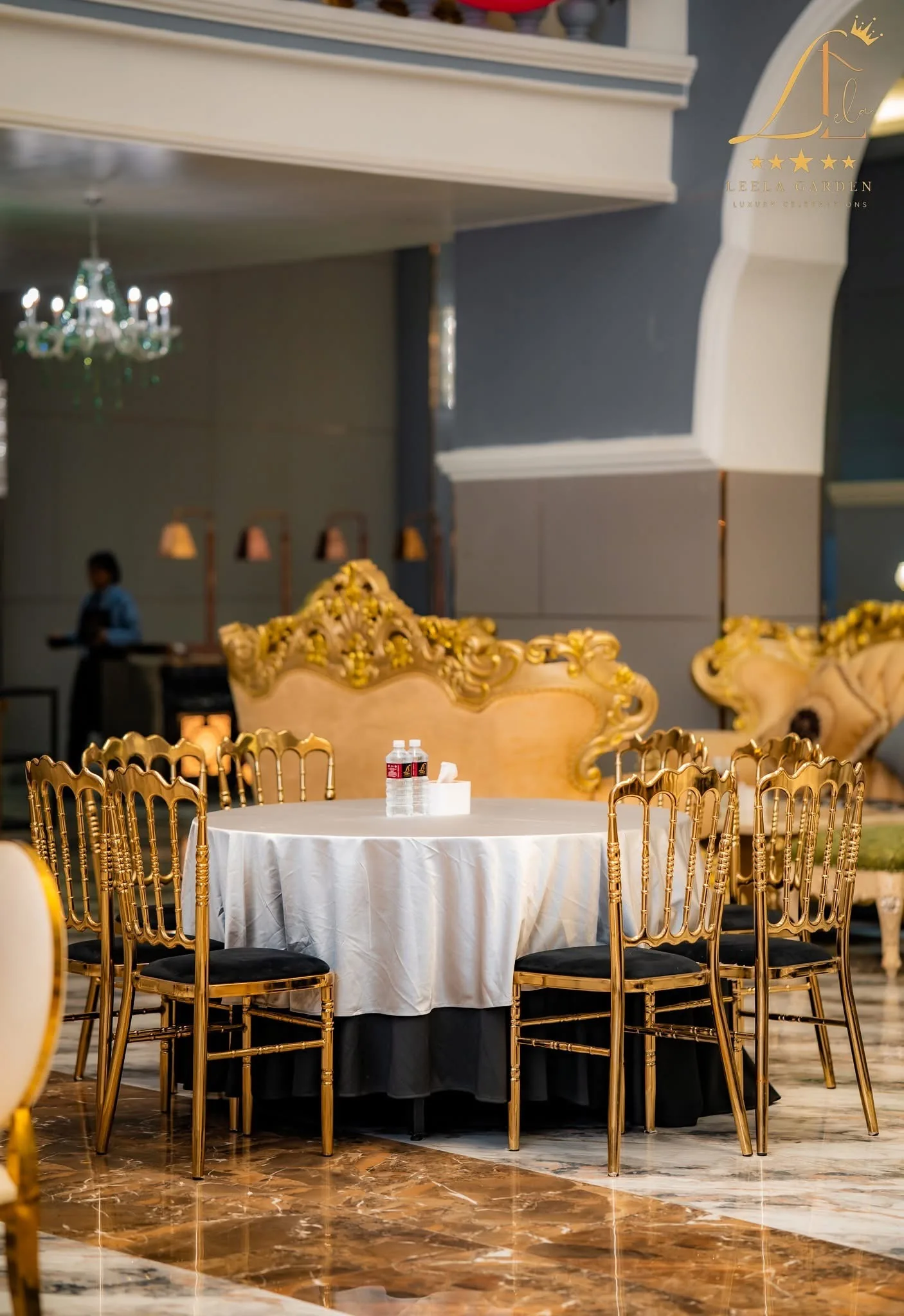 A gilded baroque settee behind a linen-dressed round table ringed with gold chiavari chairs.