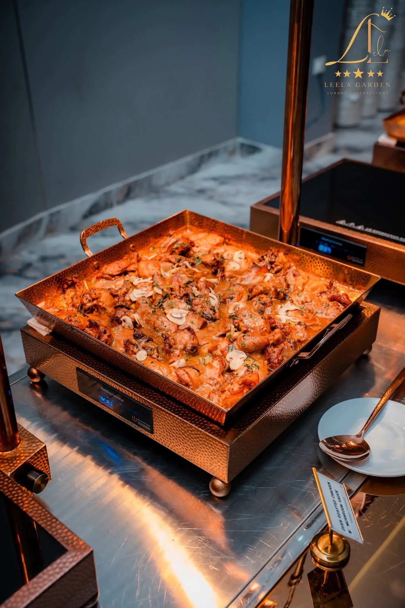 A copper tray of chicken in a dark sauce, a ladle resting beside it.