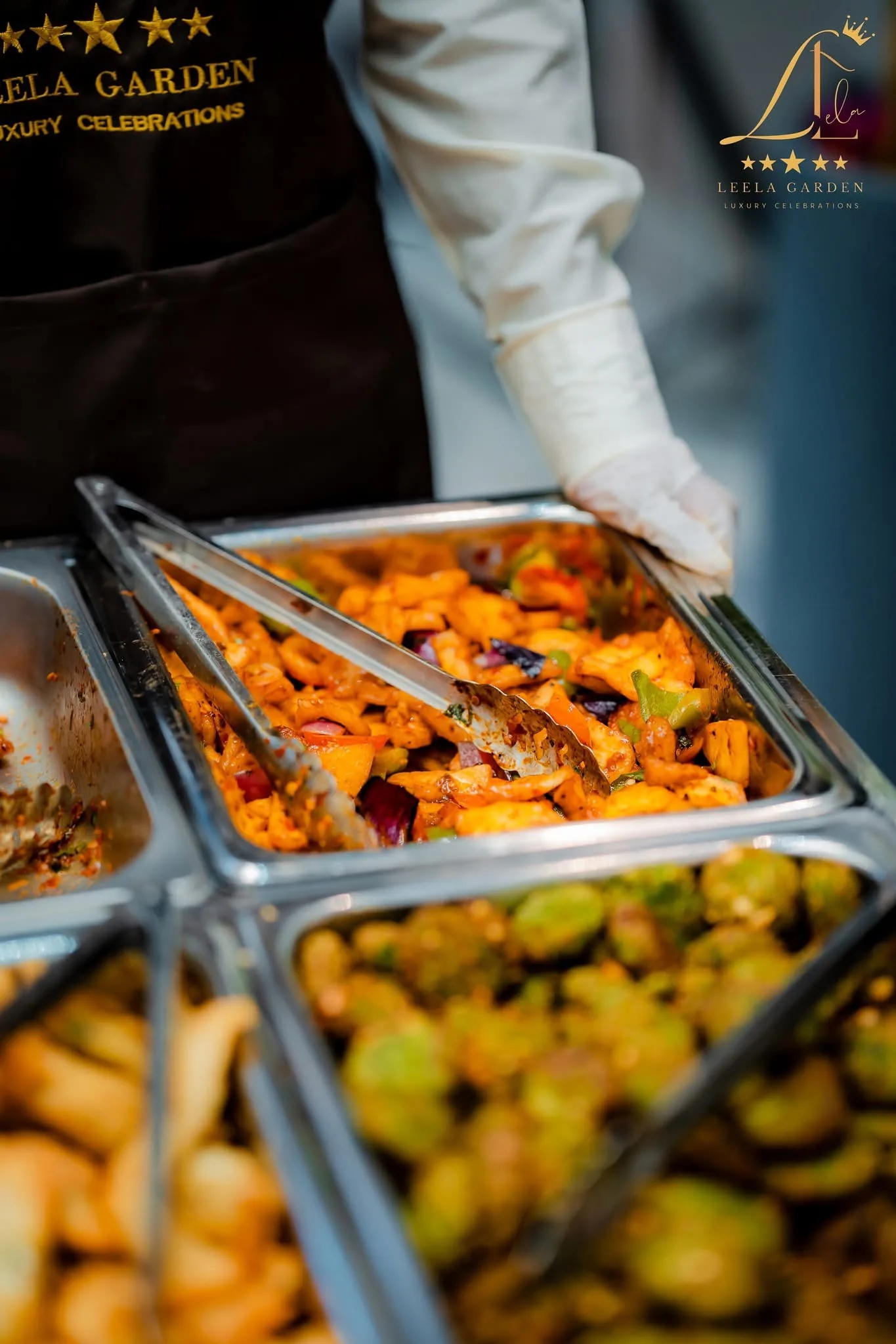 A gloved hand serving from a chafing dish with tongs.