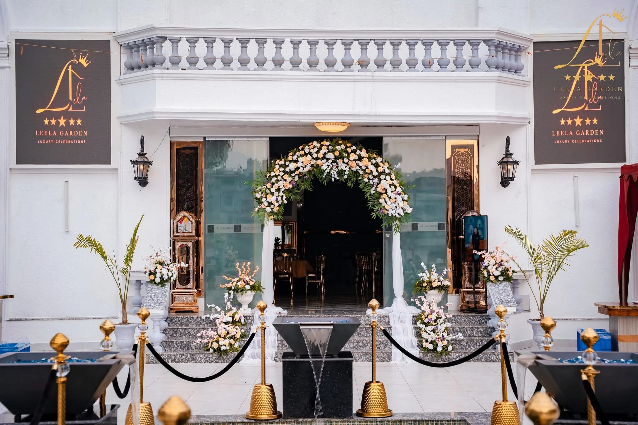 The entrance doorway framed by a tall white floral arch, gold stanchions marking the walkway.