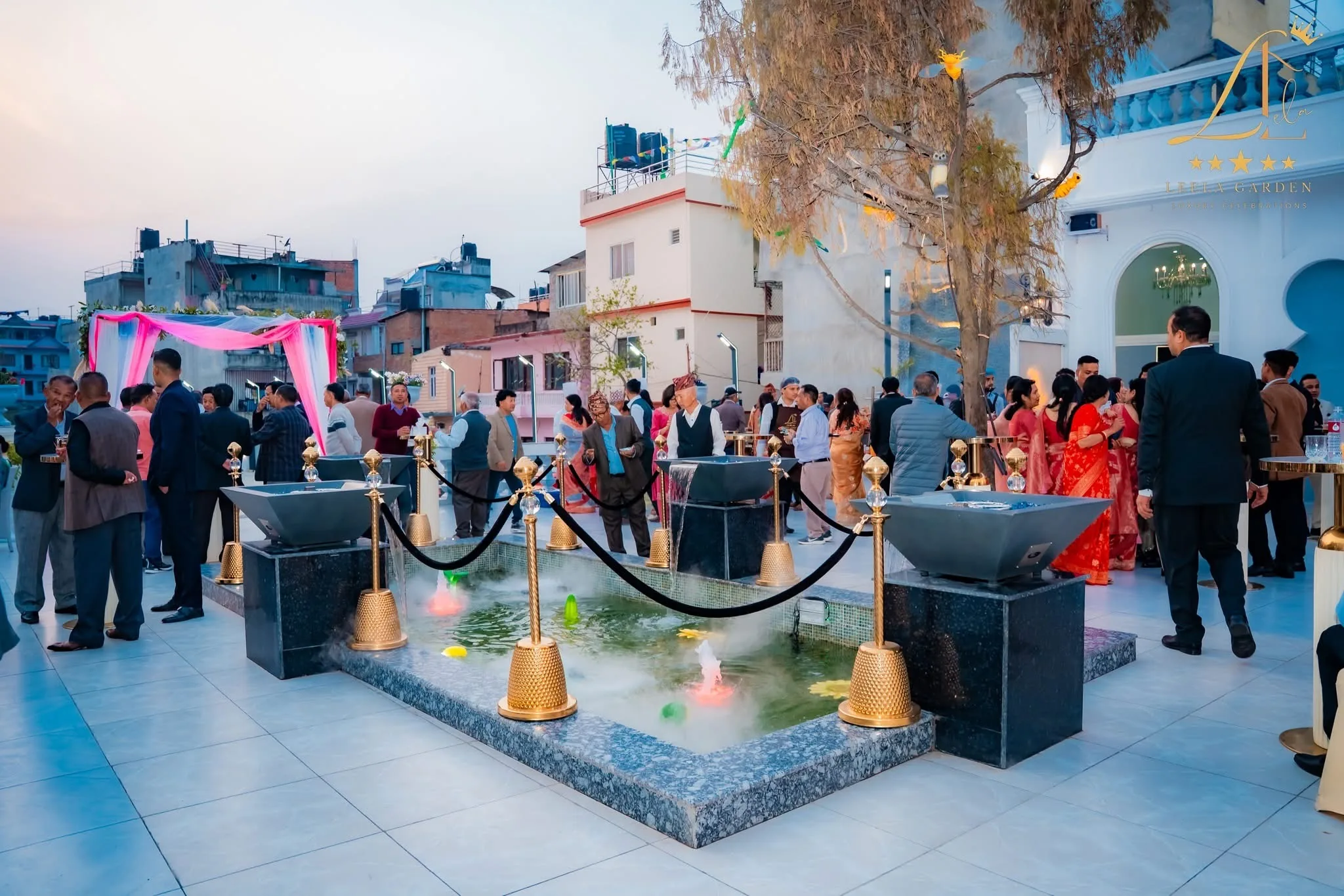 A tiled water feature in the courtyard, ringed by gold posts and rope, with the lit building behind.