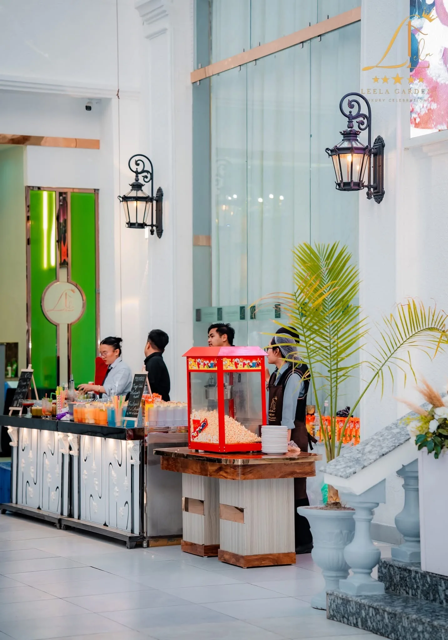 A live counter with staff and a red popcorn cart, palms against a green wall.