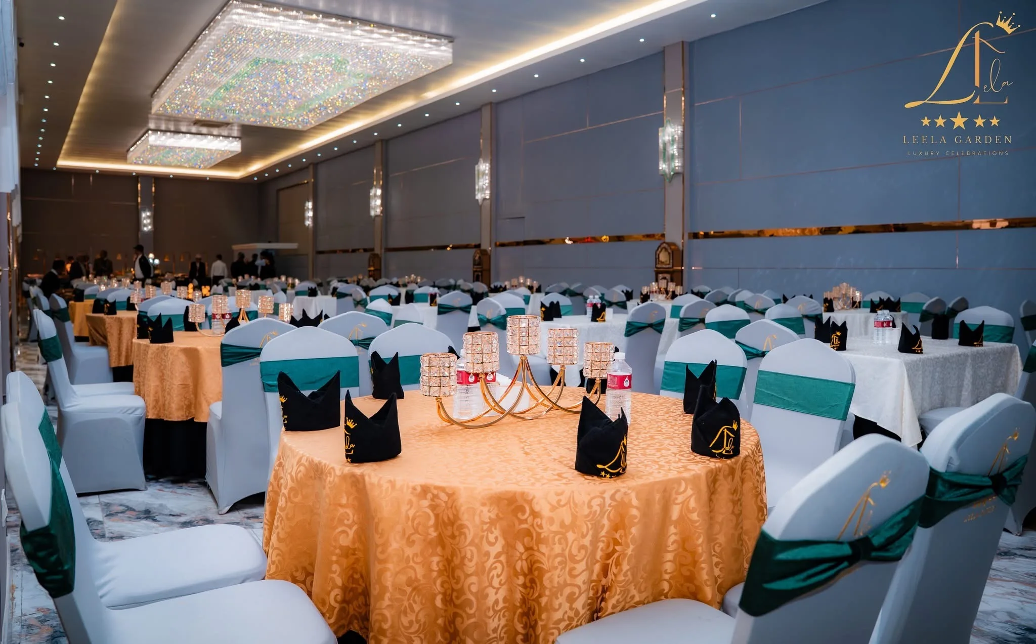 A round table under gold cloth with teal chair sashes, the set hall stretching behind it.