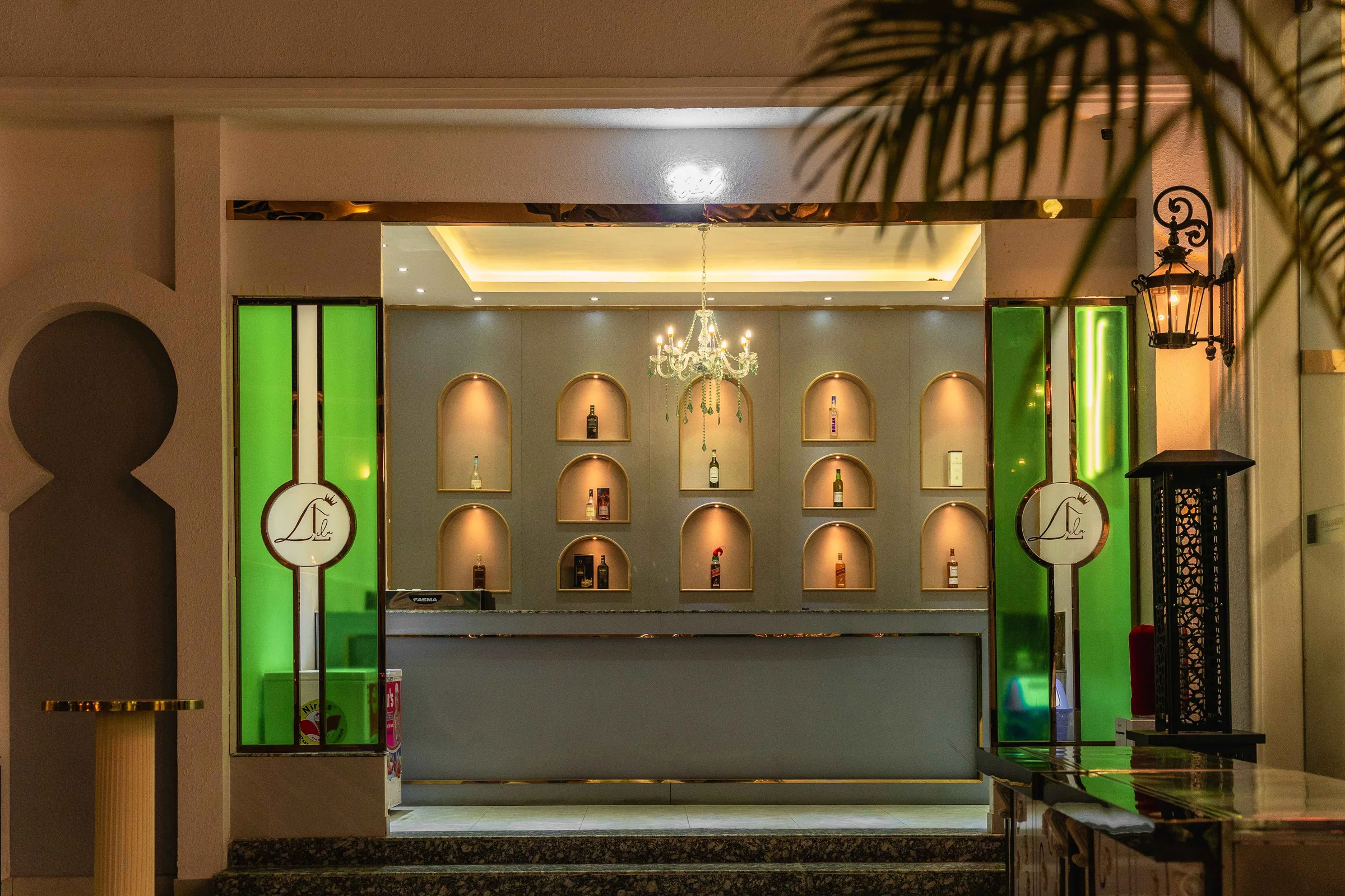 The bar counter under a chandelier, flanked by backlit arched display niches.