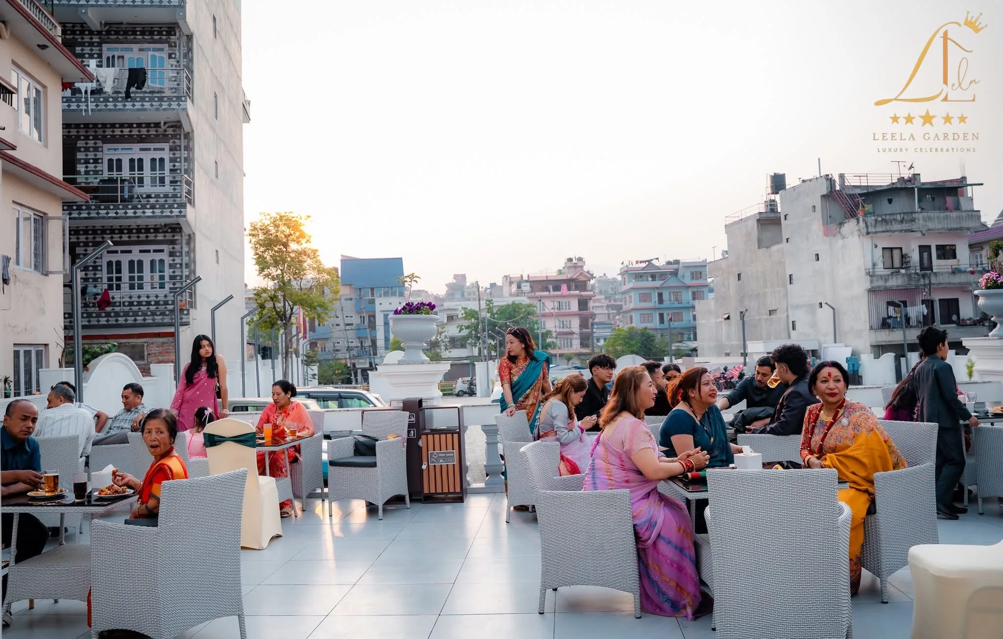 Guests seated in woven chairs on the open-air terrace at dusk, the city skyline beyond.