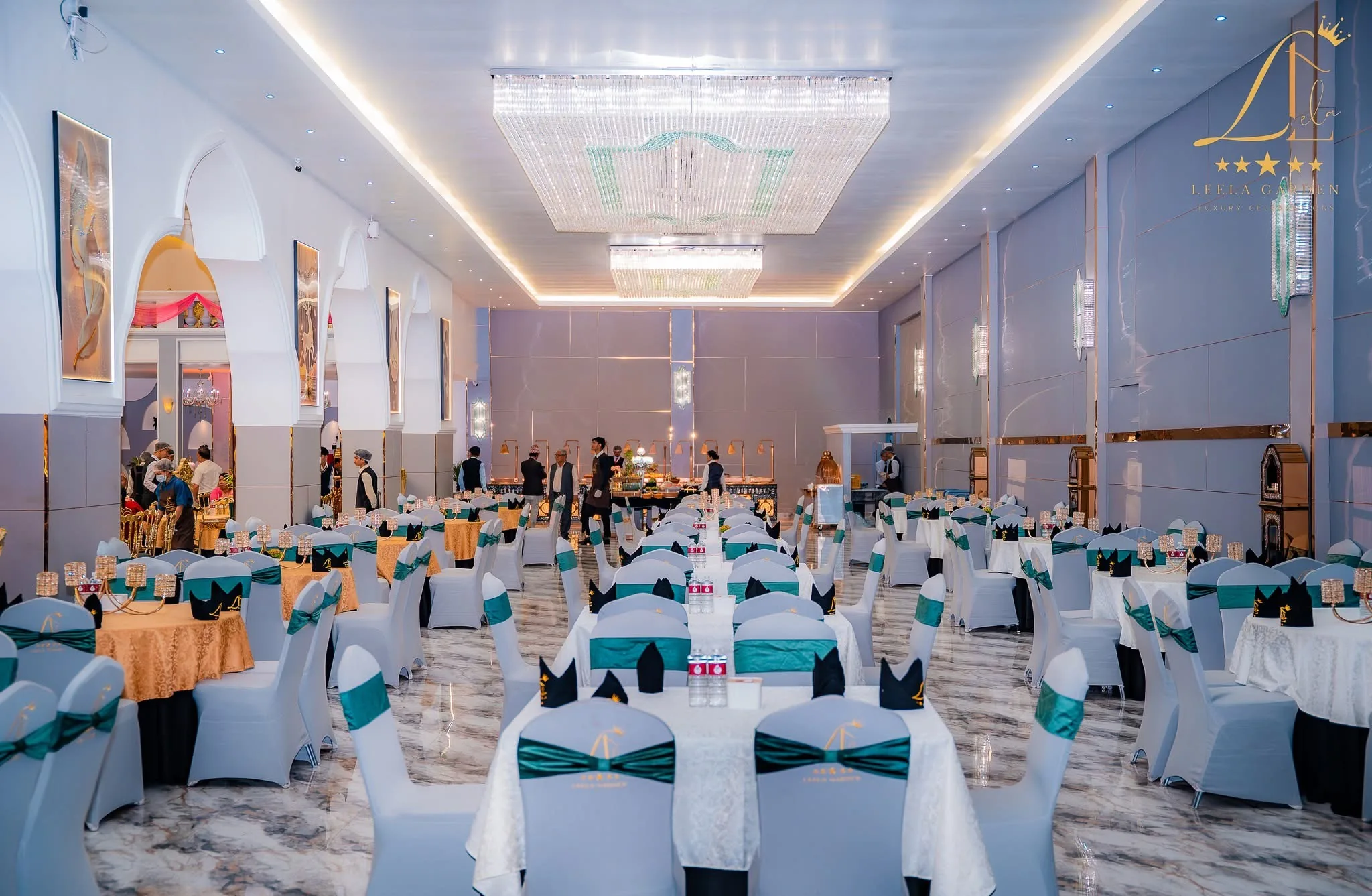 The length of the hall set for dinner, chairs in white covers with teal sashes.